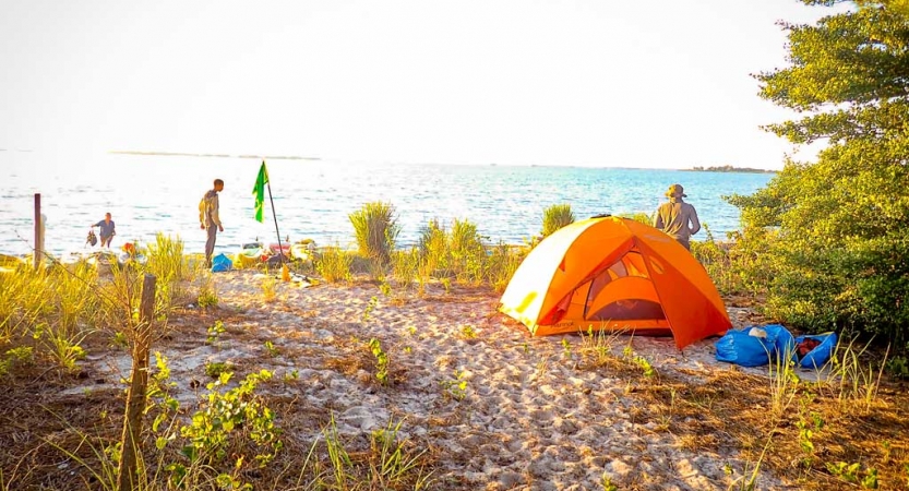 an orange tent rests in the sand at a campsite on the beach on an outward bound kayaking course